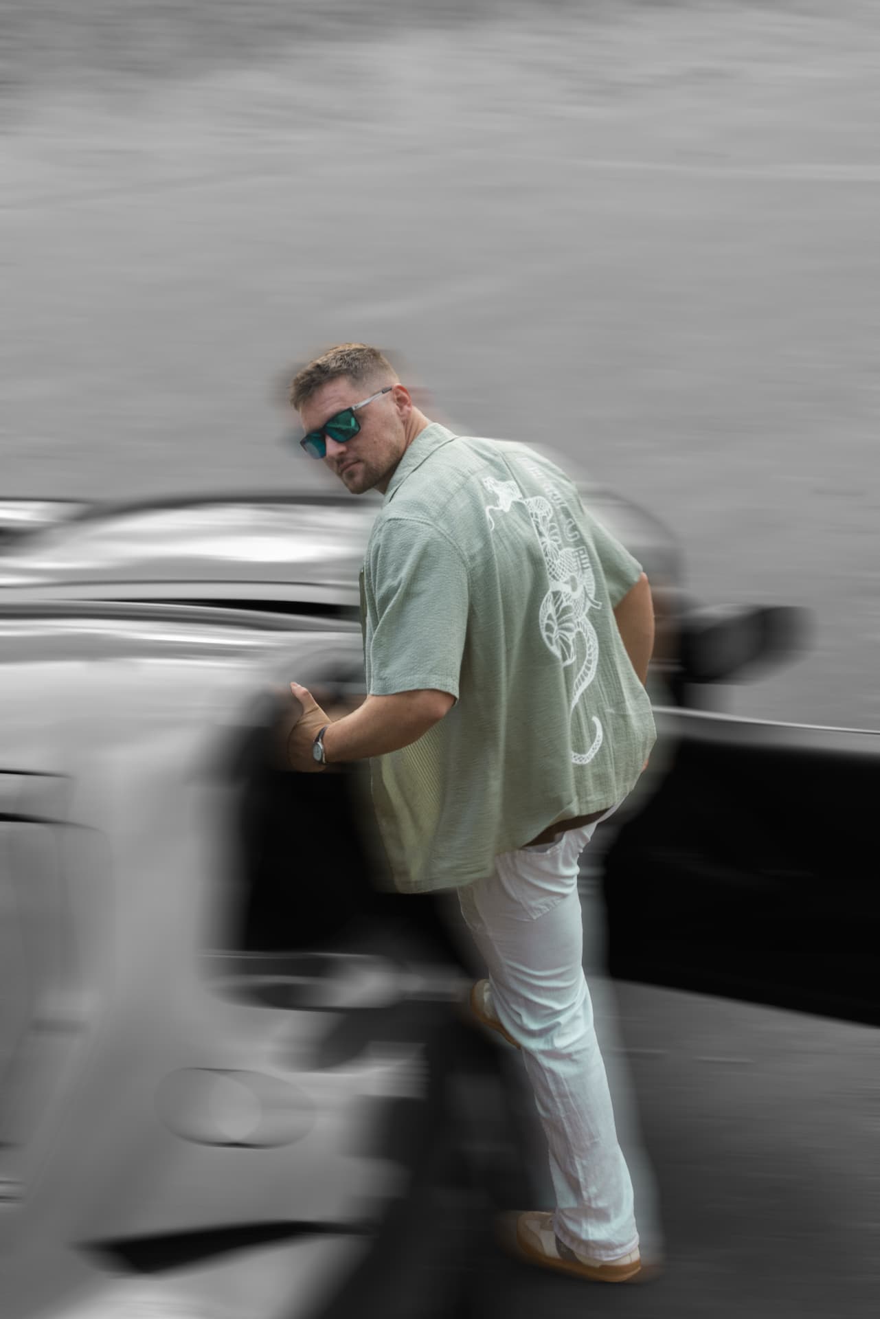 Man in a mint-green shirt with a dragon print stepping out of a Ferrari