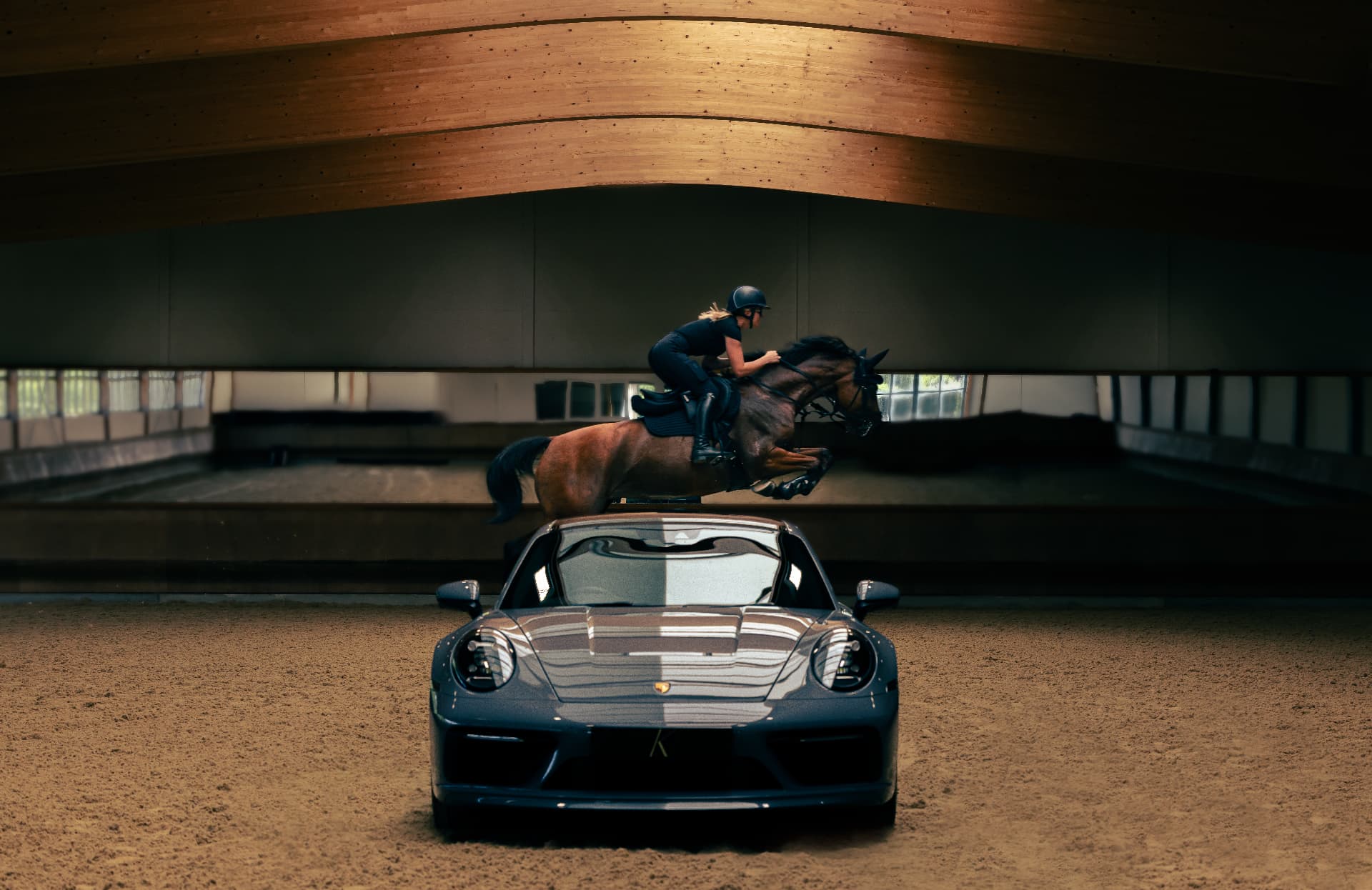 Horse jumping over a Porsche in an indoor equestrian arena